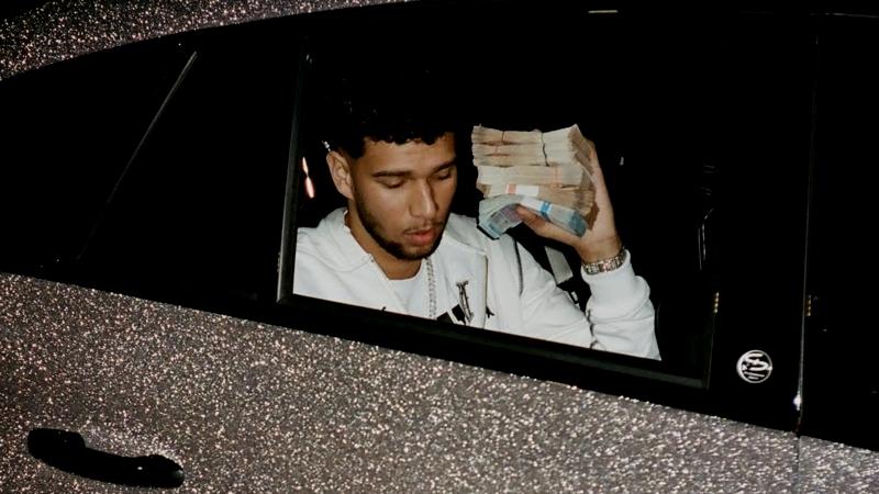 Lucio 1 0 1 sitzt in einem glitzernden Auto und zeigt einen Bündel Geldscheine aus dem Fenster