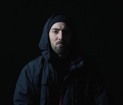 Bild des Künstlers "Accid1" in schwarzer Kapuzenjacke vor schwarzem Hintergrund.