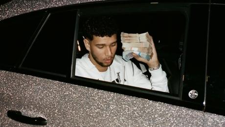 Lucio 1 0 1 sitzt in einem glitzernden Auto und zeigt einen Bündel Geldscheine aus dem Fenster