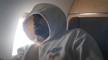 Ali As sitzt in einem weißen Hoodie in einem Flugzeug