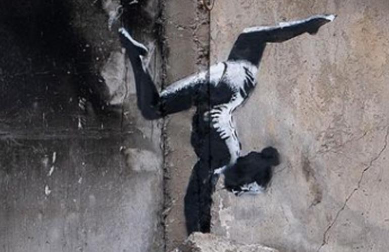 Bild des Künstlers Banksy. Darauf zu sehen ist ein Mädchen, das auf Trümmern einen Handstand macht